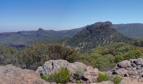 Expansive view past rocky outcrops to a rugged landscape of peaks and valleys clad in natural vegetation.. Photo &copy; Jessica Stokes