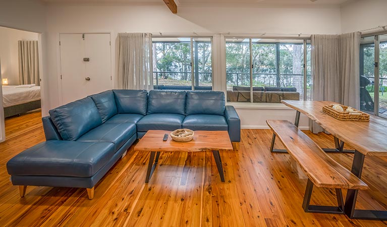 Judges House living room, with couch, coffee table and dining table with bench, Murramarang National Park. Photo: John Spencer &copy;DPIE