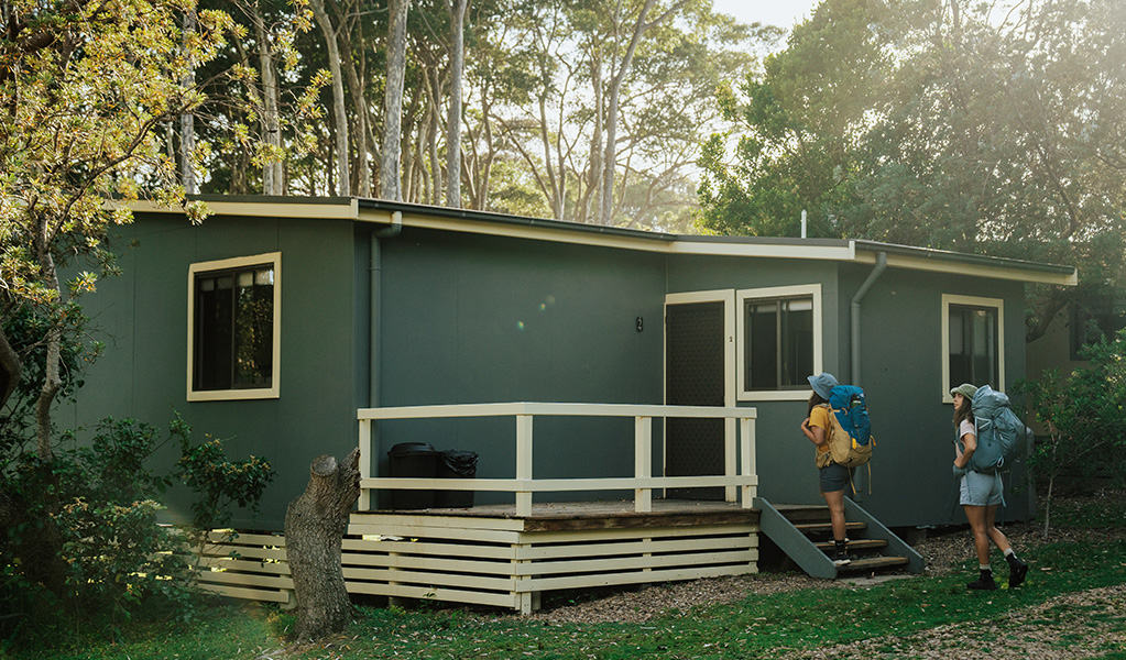 2 walkers climbing the steps to their hard-roof accommodation, at Depot Beach cabins in Murramarang National Park. Photo: Remy Brand &copy; Remy Brand