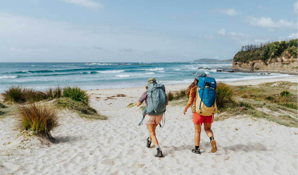 2 bushwalkers walking across Pretty Beach toward the sea. Credit: Remy Brand © Remy Brand