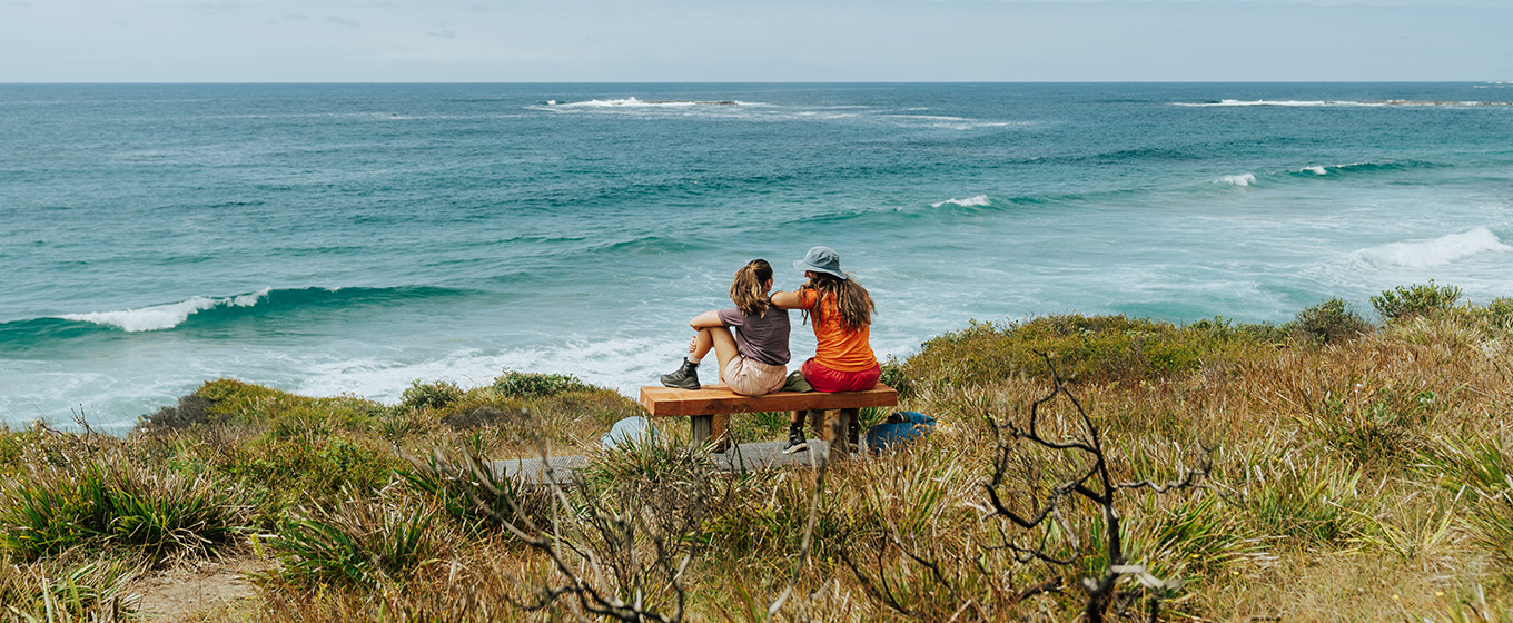 2 walkers sitting on a bench on the walking track between Pretty Beach and Pebbly Beach, watching the sea. Credit: Remy Brand © Remy Brand