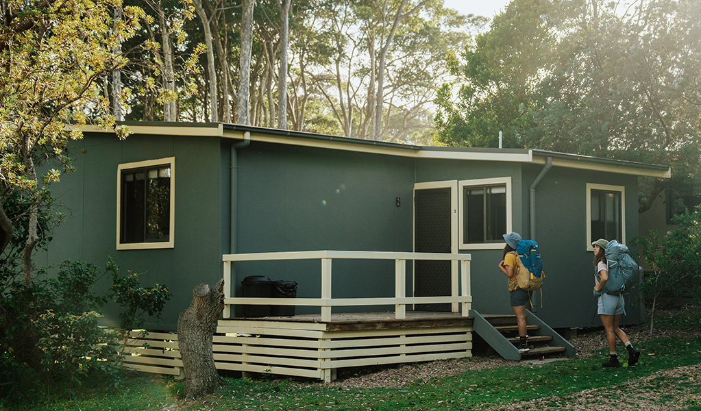 2 walkers climbing the steps to their hard-roof accommodation, at Depot Beach cabins in Murramarang National Park. Photo: Remy Brand © Remy Brand