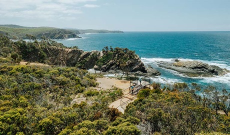 Aerial view of 2 bushwalkers standing on North Head lookout taking in the coastal scene, Murramarang National Park. Credit: Remy Brand &copy; Remy Brand