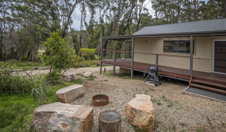 The exterior of Pebbly Beach shacks surrounded by coastal rainforest, with stone seats and fire pit. Photo: John Spencer &copy; DPIE