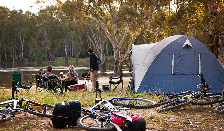 A group of friends next to their tent, with their bikes in the foreground on the banks of the river at Murray Valley campgrounds. Photo: David Finnegan &copy; DPIE