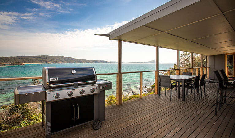 A gas barbecue and outdoor seating on the deck of Davies Cottage, with Sugarloaf Bay in the background. Photo: John Spencer &copy; DPIE