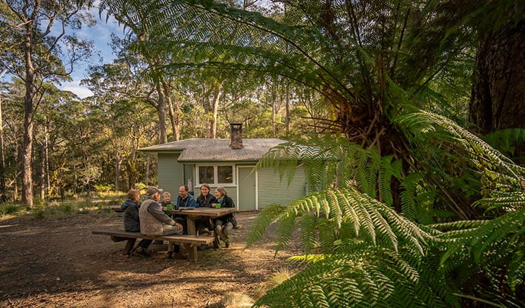 Family sitting around the picnic table outside Toms Cabin. Photo: John Spencer &copy; DPIE