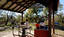 View of a woman seated at a picnic table next to a barbecue in the shade of a picnic shelter. Photo &copy; Jessica Stokes