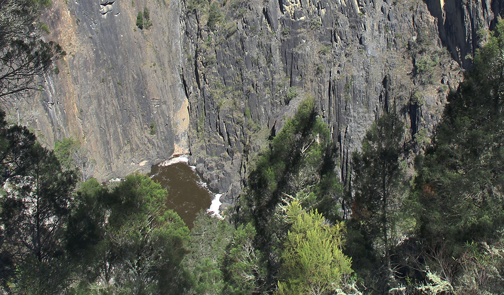 View of a pool at the base of sheer grey cliffs in a rugged wilderness setting. Photo &copy; Jessica Stokes