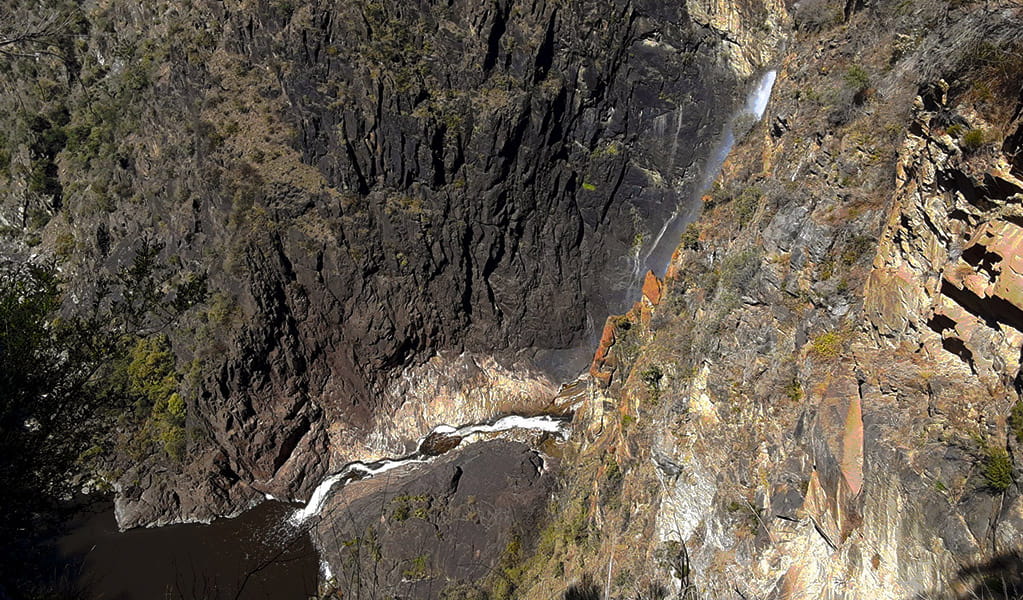 View of waterfall plunging into a gorge next to a steep cliff wall of dark-coloured rock. Photo credit: Josh Armitage &copy; DPIE