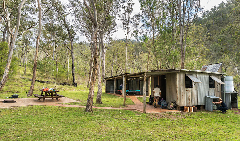 Tiny, timber Colwells Hut with a seperate building for camper stretchers and an outdoor picnic table. Credit: David Waugh © DCCEEW