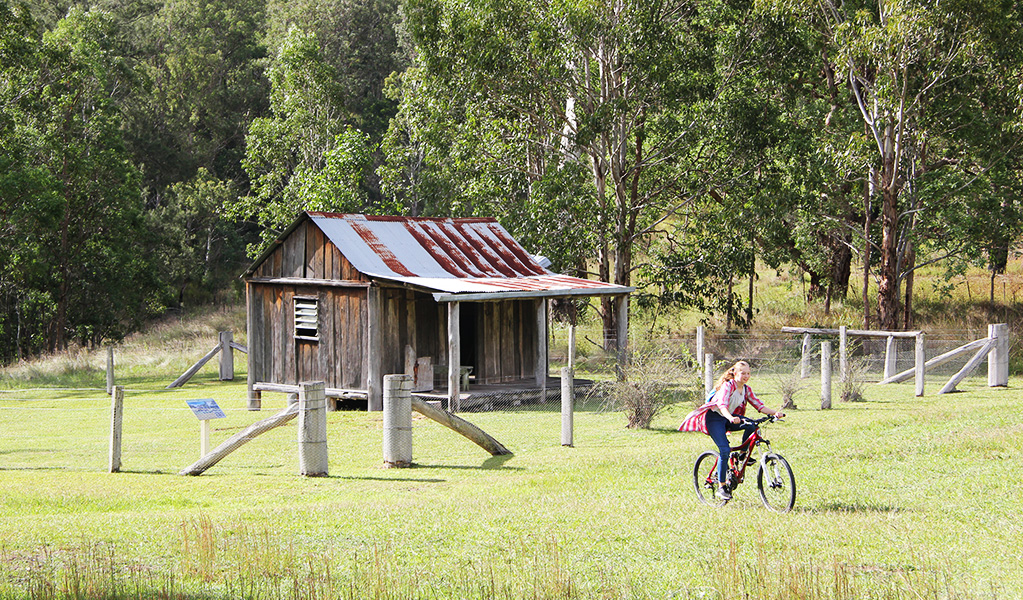 Girl rides a mountain bike in the campground paddock next to historic Youdales Hut. Credit: Natasha Webb &copy; Natasha Webb/DCCEEW