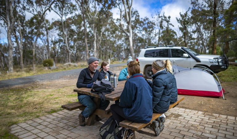 A group of friends sitting at a picnic table with their tent in the background at Dangars Gorge campground, Oxley Wild Rivers National Park. Photo: John Smith &copy; DPE