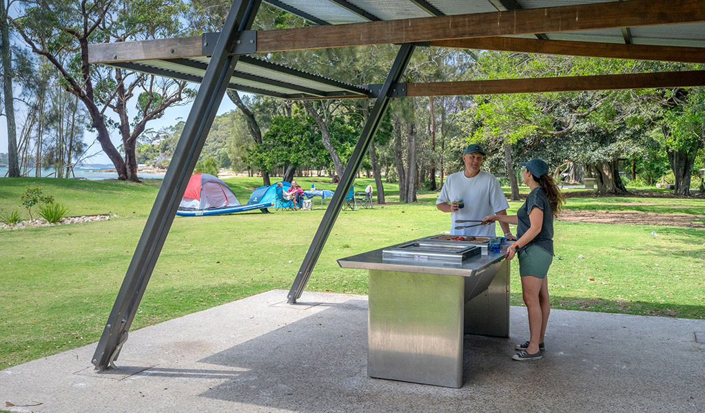 2 people using a sheltered barbecue at Bonnie Vale campground in Royal National Park. Credit: John Spencer/DCCEEW  &copy; DCCEEW