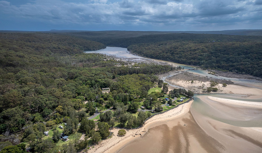 An aerial view of Bonnie Vale campground surrounded by bush and next to Hacking river and beach in Royal National Park. Credit: John Spencer/DCCEEW  &copy; DCCEEW