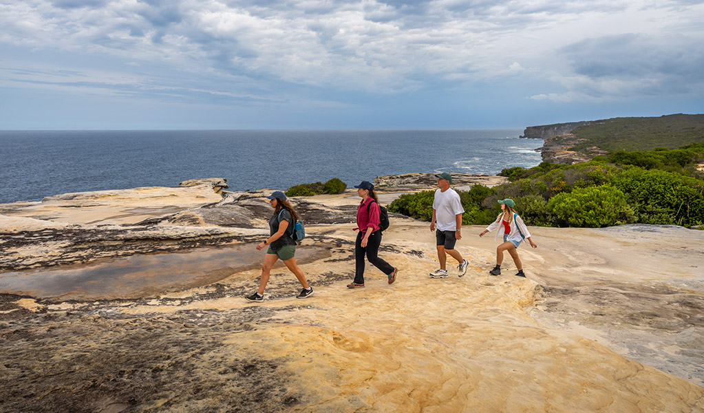 A family bushwalking on The Coast track near Bundeena, with cliffs and ocean in the distance. Credit: John Spencer © DCCEEW