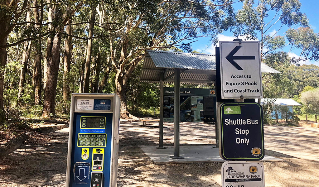 Machines to buy a day pass for Royal National Park. Shuttle bus timetable with signage and a picnic seat in the background. Credit: Natasha Webb &copy; DPIE/Natasha Webb