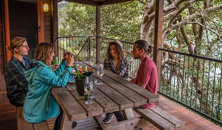 Four people drink wine at a table on the balcony of Weemalah Cottage, Royal National Park. Photo: John Spencer/OEH