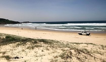 View across dunes to people and a vehicle on Samurai Beach and a distant headland. Photo: Jim Cutler &copy; DPIE