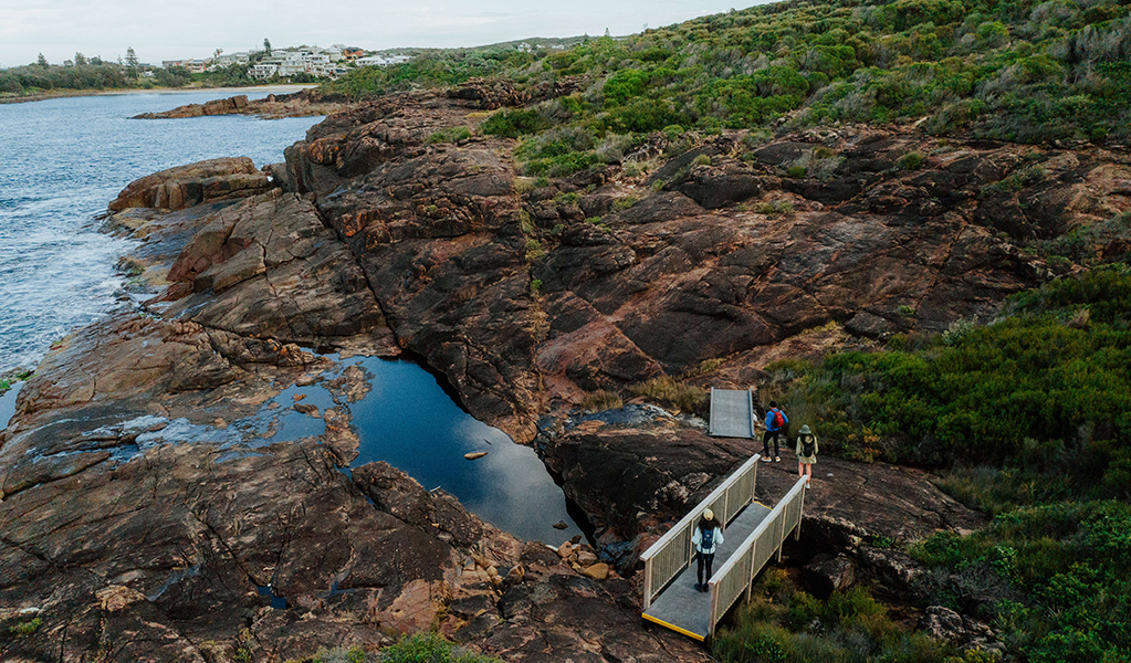 Aerial photo of walkers crossing a small bridge over a coastal rock platform near the village of Boat Harbour. Credit: Daniel Parsons &copy; Daniel Parsons