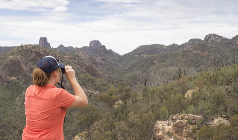 A woman takes photos of rugged mountains and spires stretching into the distance. Photo: Leah Pippos &copy; DPIE