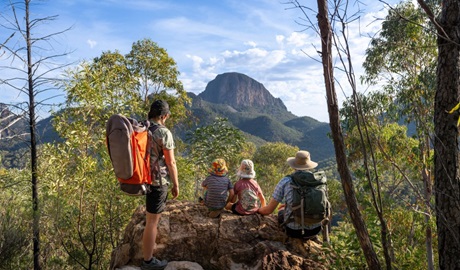 A family sitting on a rock looking out towards the peaks and spires of the Warrumbungles on Fans Horizon walking track in Warrumbungle National Park. Photo: john Spencer &copy; DCCEEW