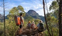 A family sitting on a rock looking out towards the peaks and spires of the Warrumbungles on Fans Horizon walking track in Warrumbungle National Park. Photo: john Spencer &copy; DCCEEW