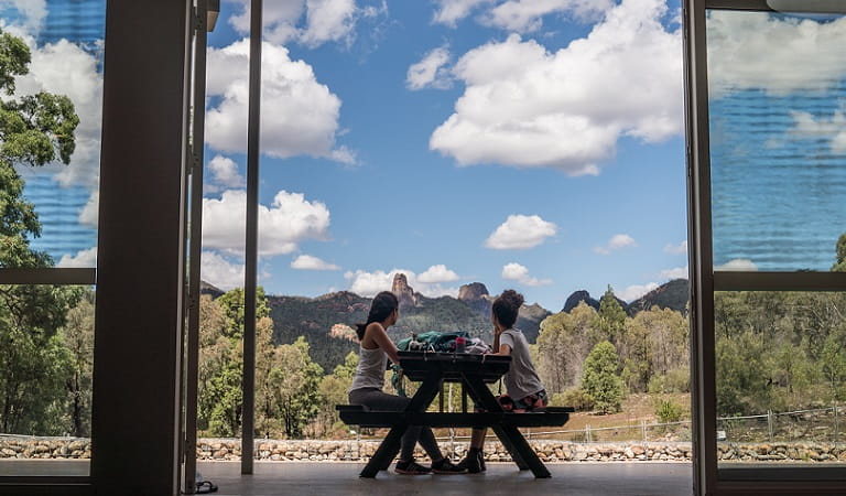 Two friends rest at an outside table at Warrumbungle Visitor Centre, admiring the view of the grand High Tops mountains in Warrumbungle National Park. Photo &copy; Robert Mulally