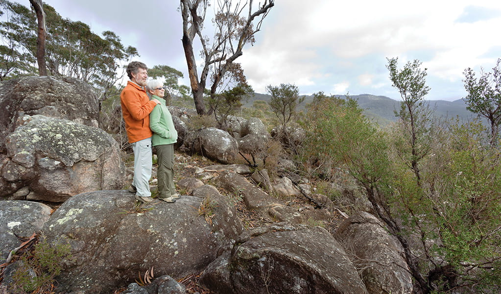 A couple stands on a rocky outcrop set in the dry forests of Washpool National Park. Photo credit: Rob Cleary &copy; DPIE