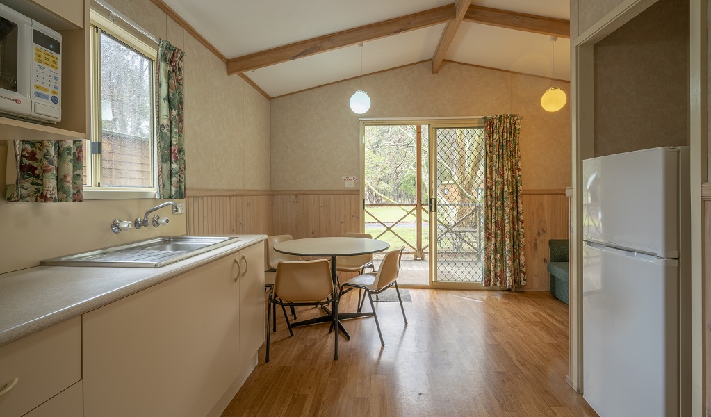 Inside one of the Wombeyan Caves cabins, showing the kitchen, dining table and open sliding glass door. Photo: John Spencer. &copy; DCCEEW