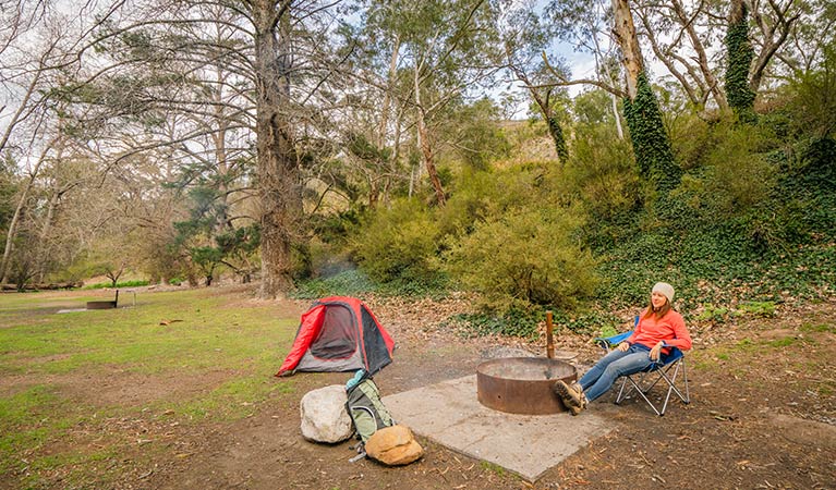 Camper sitting by the fire in a fire ring at Wombeyan Caves campground. Photo: John Spencer/OEH