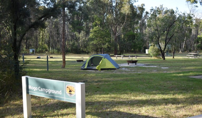 A sign at Mogo campground with a tent and woodfire barbecues in the background at Yengo National Park. Photo: Sarah Brookes &copy; DPIE