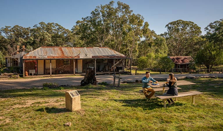 A couple enjoying morning tea at the picnic table outside The Bank Room in Yerranderie Regional Park. Photo: John Spencer/OEH