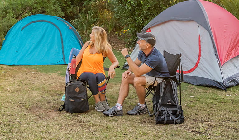 2 campers sitting with their backpacks with their tents set up in the background. Photo: John Spencer/DPIE