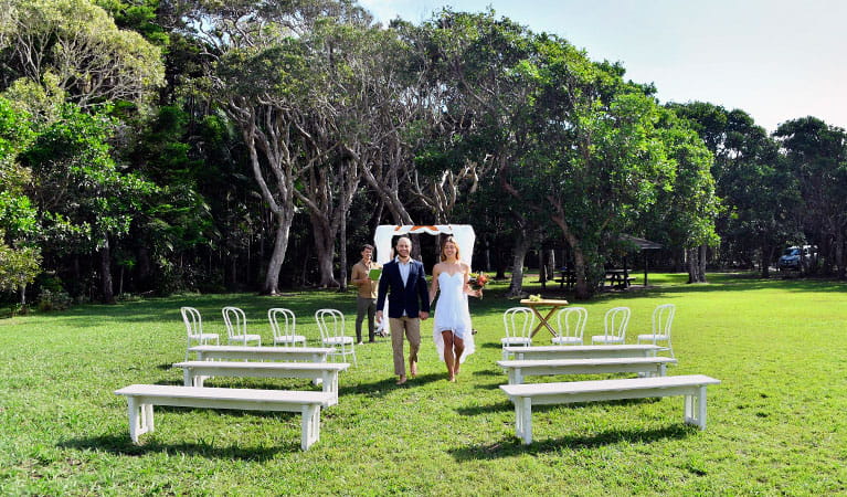 A couple walking down the aisle after their wedding ceremony at Broken Head lawn. Photo: Fiora Sacco &copy; DPIE