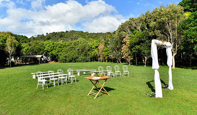 Chairs, a table and a bridal arch set up on Broken Head lawn with lush rainforest in the background in Broken Head Nature Reserve. Photo: Fiora Sacco &copy; DPIE