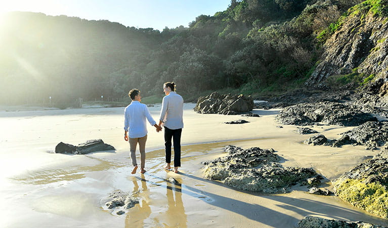 A couple walking hand-in-hand along the sand at Tallow Beach in Cape Byron State Conservation Area. Photo: Fiora Sacco &copy; DPIE
