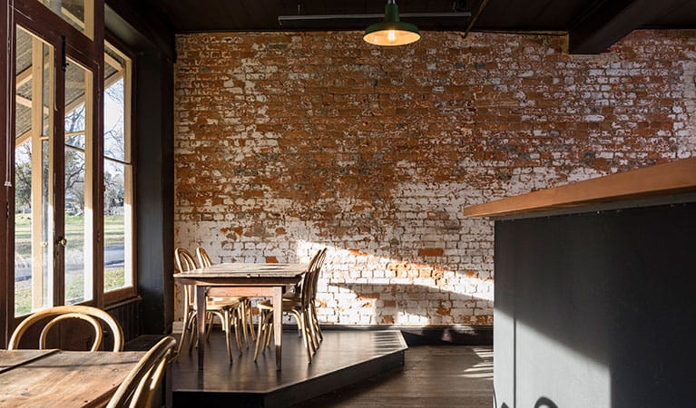 Tables and chairs next to the window with an exposed brick wall in the background at Hosies in Hill End Historic Site. Photo:  Jennifer Leahy &copy; DPE