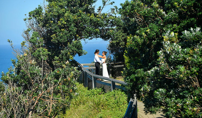 A couple standing under a natural arch created by trees at Most Easterly Point in Cape Byron State Conservation Area. Photo: Fiora Sacco &copy; DPIE