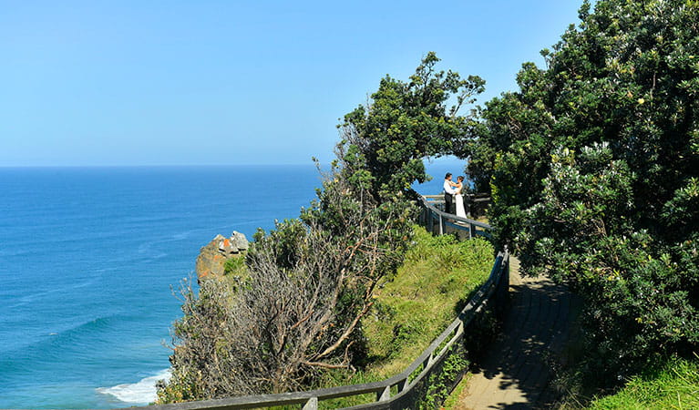 A couple standing under a natural arch created by trees at Most Easterly Point in Cape Byron State Conservation Area. Photo: Fiora Sacco &copy; DPIE