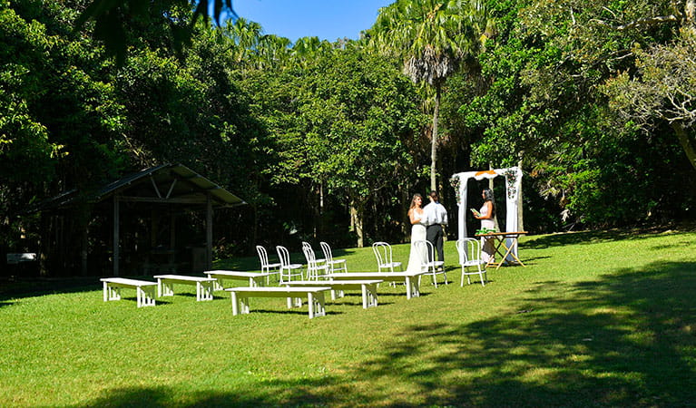 A couple saying their vows under a wedding arch on Palm Valley lawn in Cape Byron State Conservation Area. Photo: Fiora Sacco &copy; DPIE