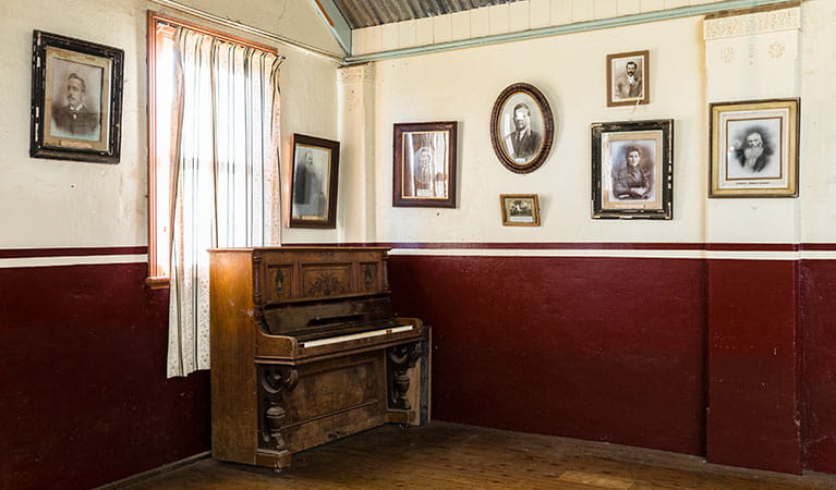 Historic photographs on the walls behind a piano in Royal Hall, Hill End Historic SIte. Photo: Jennifer Leahy &copy; DPE