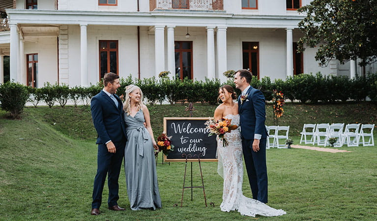 A couple with a bridesmaid and groomsman standing next to a wedding welcome sign on the lawn of Strickland Estate. Photo &copy; Matt Horspool 