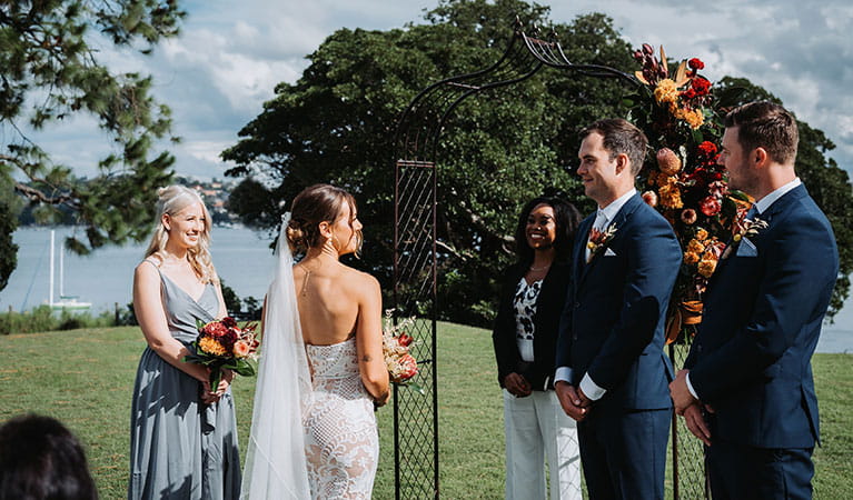 A wedding party in front of a bridal arch, overlooking Sydney Harbour at Strickland Estate. Photo &copy; Matt Horspool
