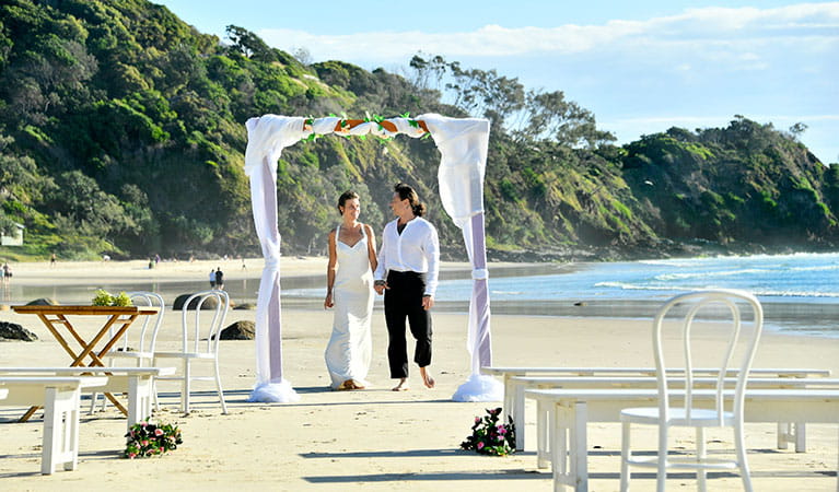 A couple under a wedding arch on Wategos Beach in Cape Byron State Conservation Area. Photo: Fiora Sacco &copy; DPIE