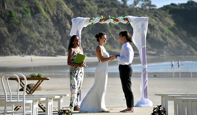 A couple saying their vows beneath a wedding arch on Wategos Beach in Cape Byron State Conservation Area. Photo: Fiora Sacco &copy; DPIE