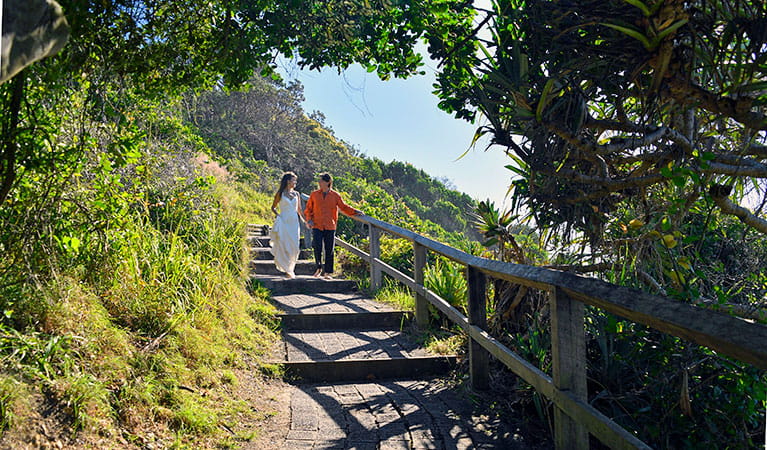 A couple walking down the stairs along a walkway overlooking Wategos Beach in Cape Byron State Conservation Area. Photo: Fiora Sacco &copy; DPIE