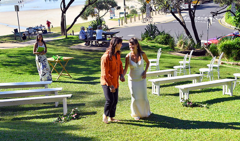 A joyful couple walking down the aisle after their wedding ceremony on Wategos lawn in Cape Byron State Conservation Area. Photo: Fiora Sacco &copy; DPIE